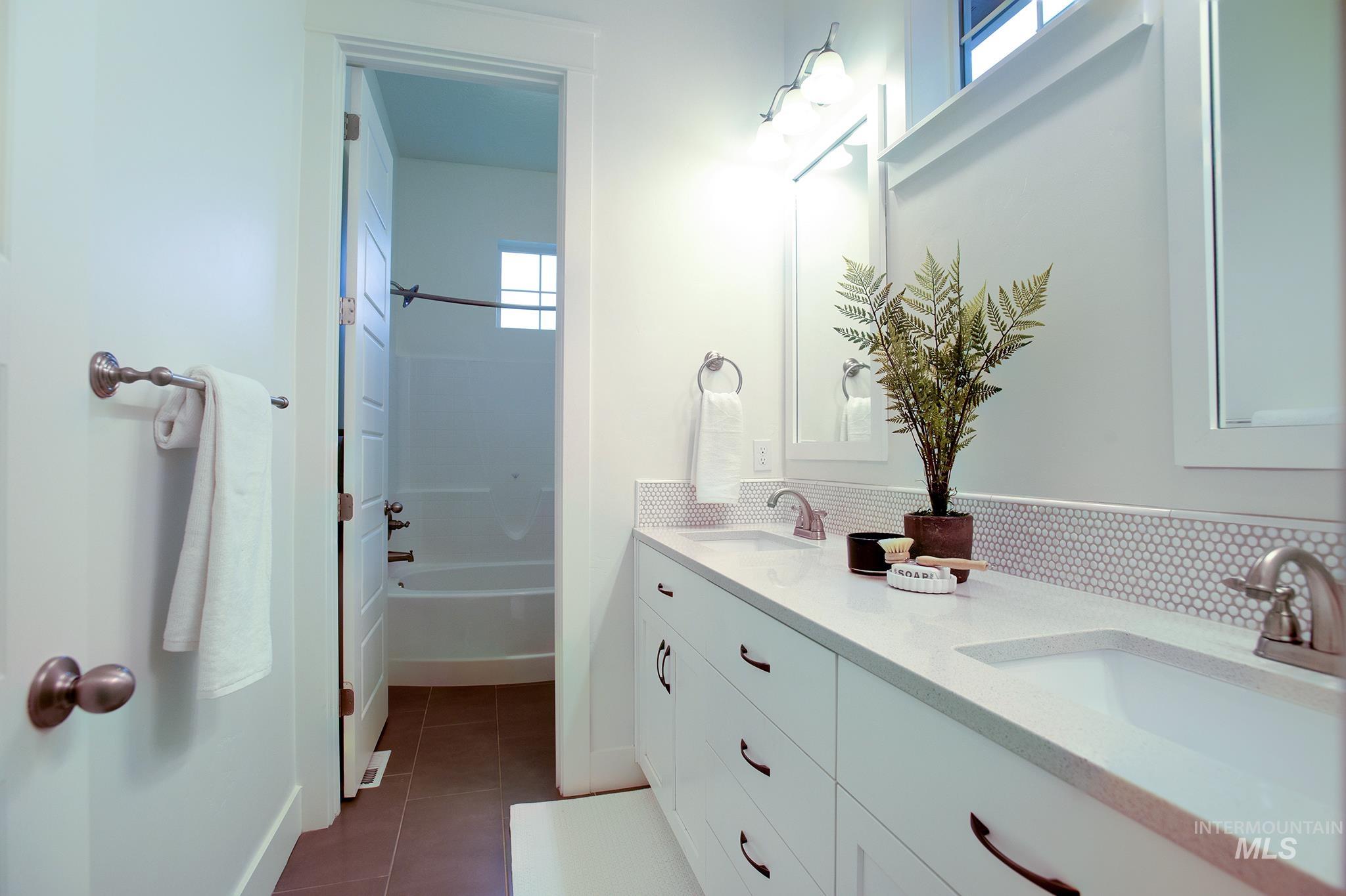 Full bathroom featuring double vanity, dark tile patterned flooring, backsplash, and bathing tub / shower combination
