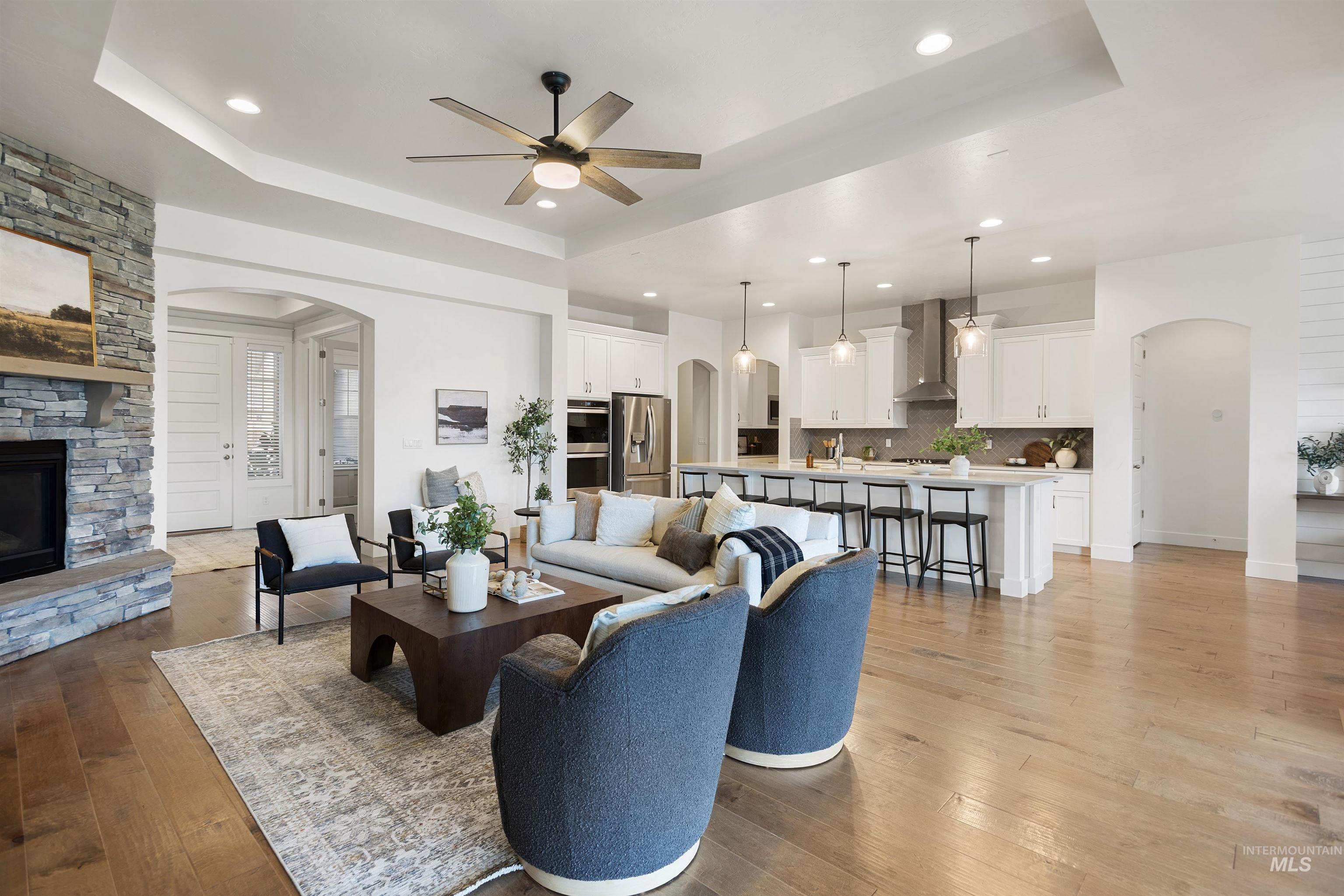 Living area with arched walkways, a fireplace, light wood-type flooring, a tray ceiling, and recessed lighting