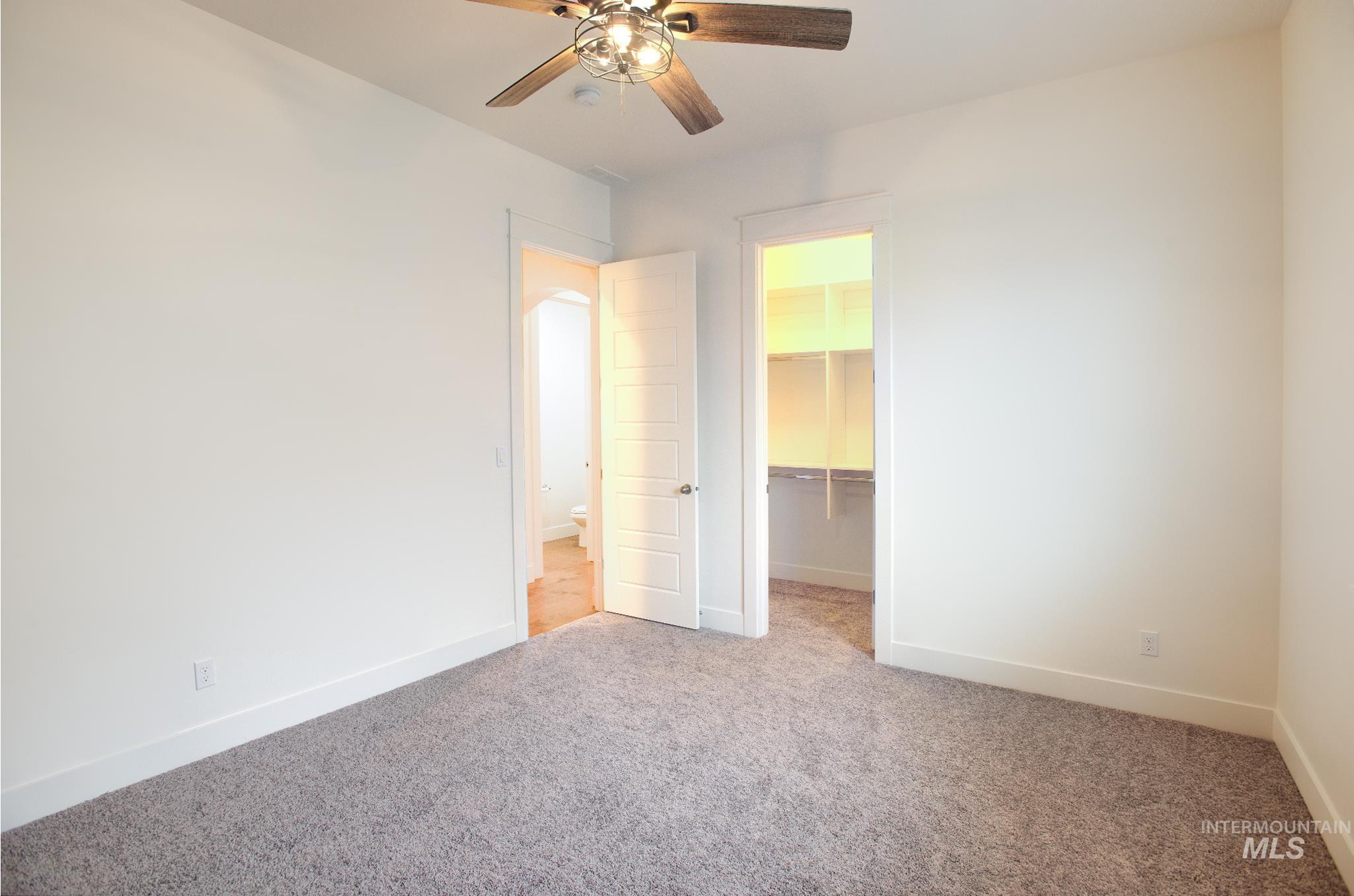 Unfurnished bedroom featuring a walk in closet, carpet flooring, and ceiling fan