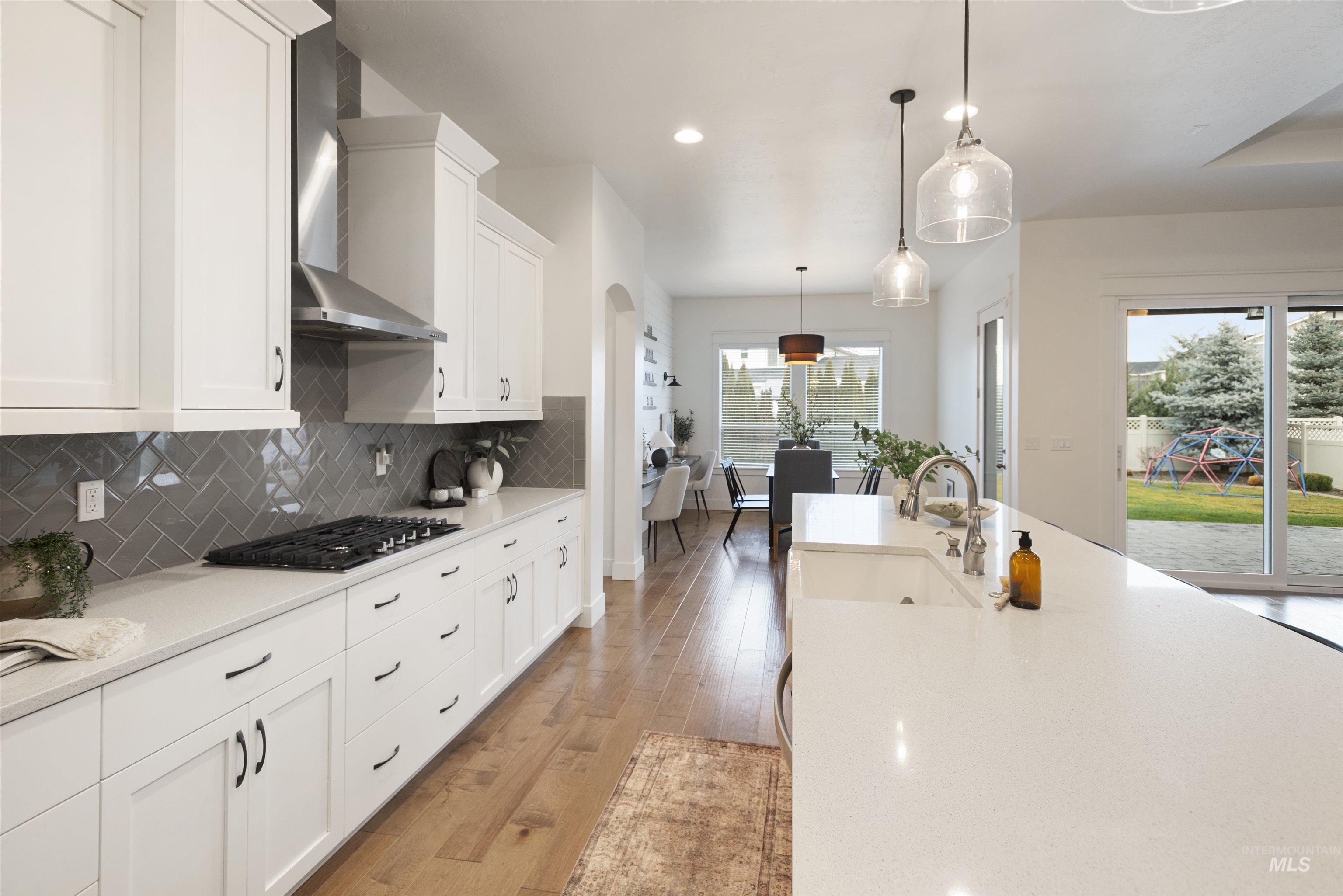 Kitchen featuring white cabinetry, decorative light fixtures, wall chimney exhaust hood, tasteful backsplash, and light stone counters