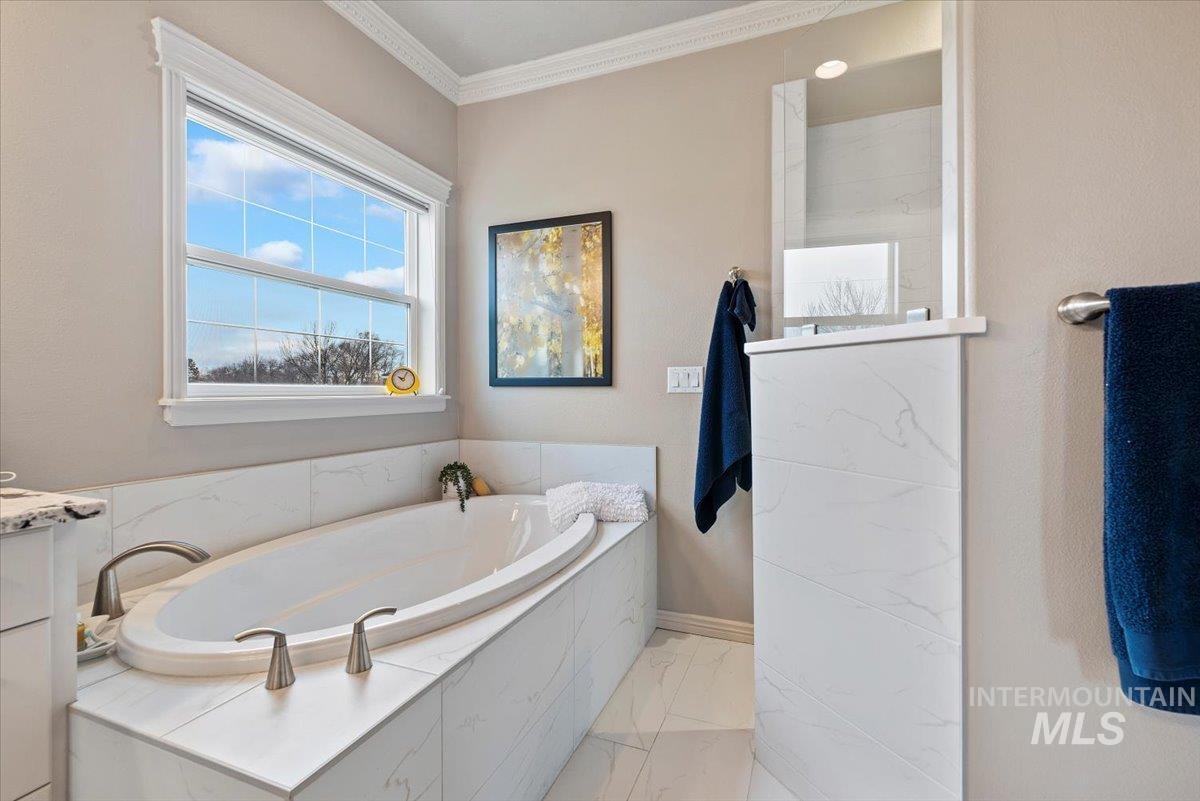 Bathroom with a bath, light marble finish flooring, ornamental molding, and vanity