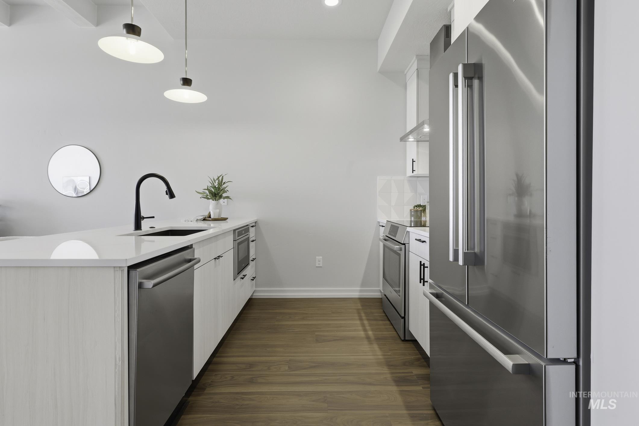 Kitchen featuring a peninsula, stainless steel appliances, white cabinets, light stone countertops, and dark wood-type flooring