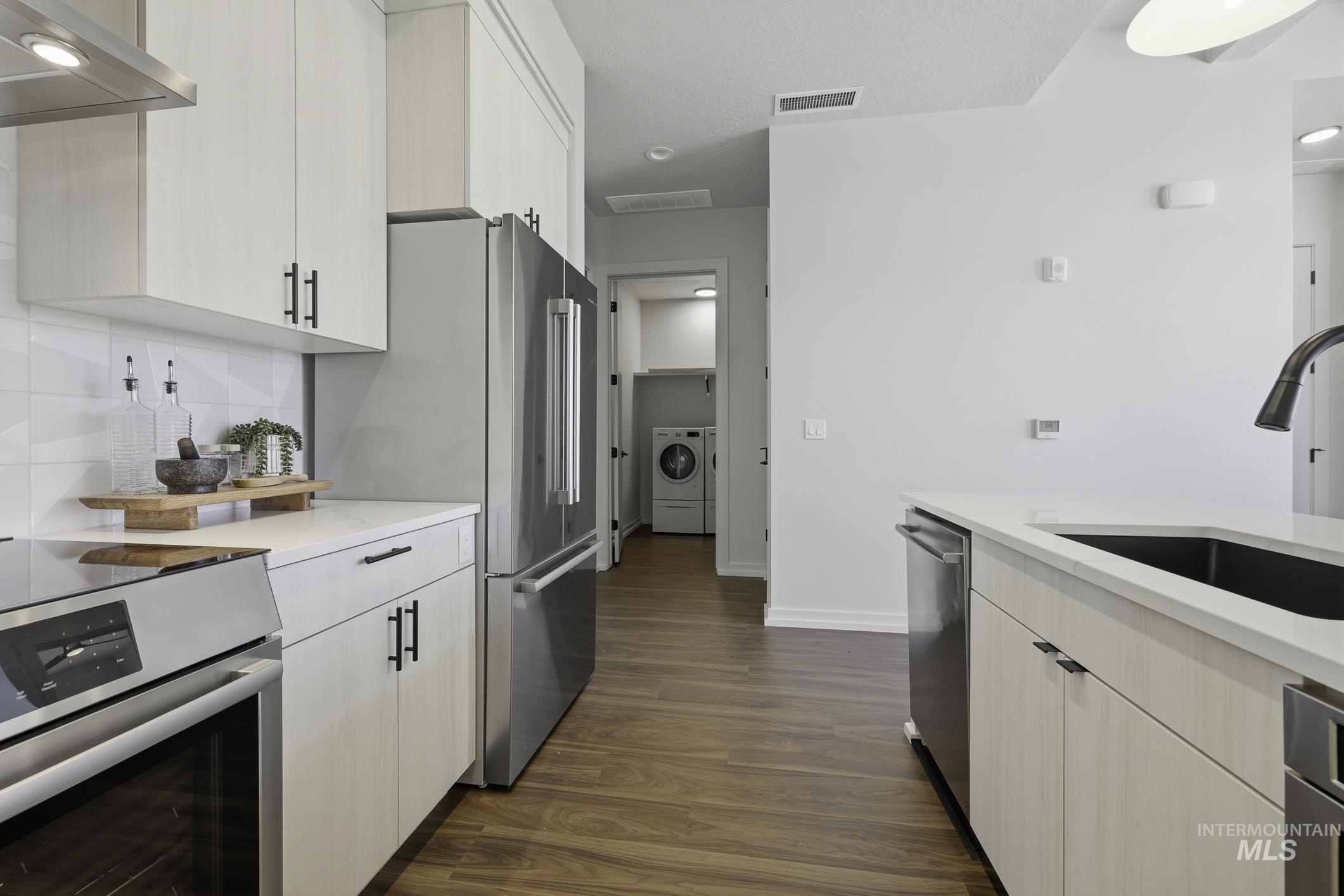 Kitchen featuring stainless steel appliances, dark wood-style floors, white cabinets, washer / dryer, and light stone counters