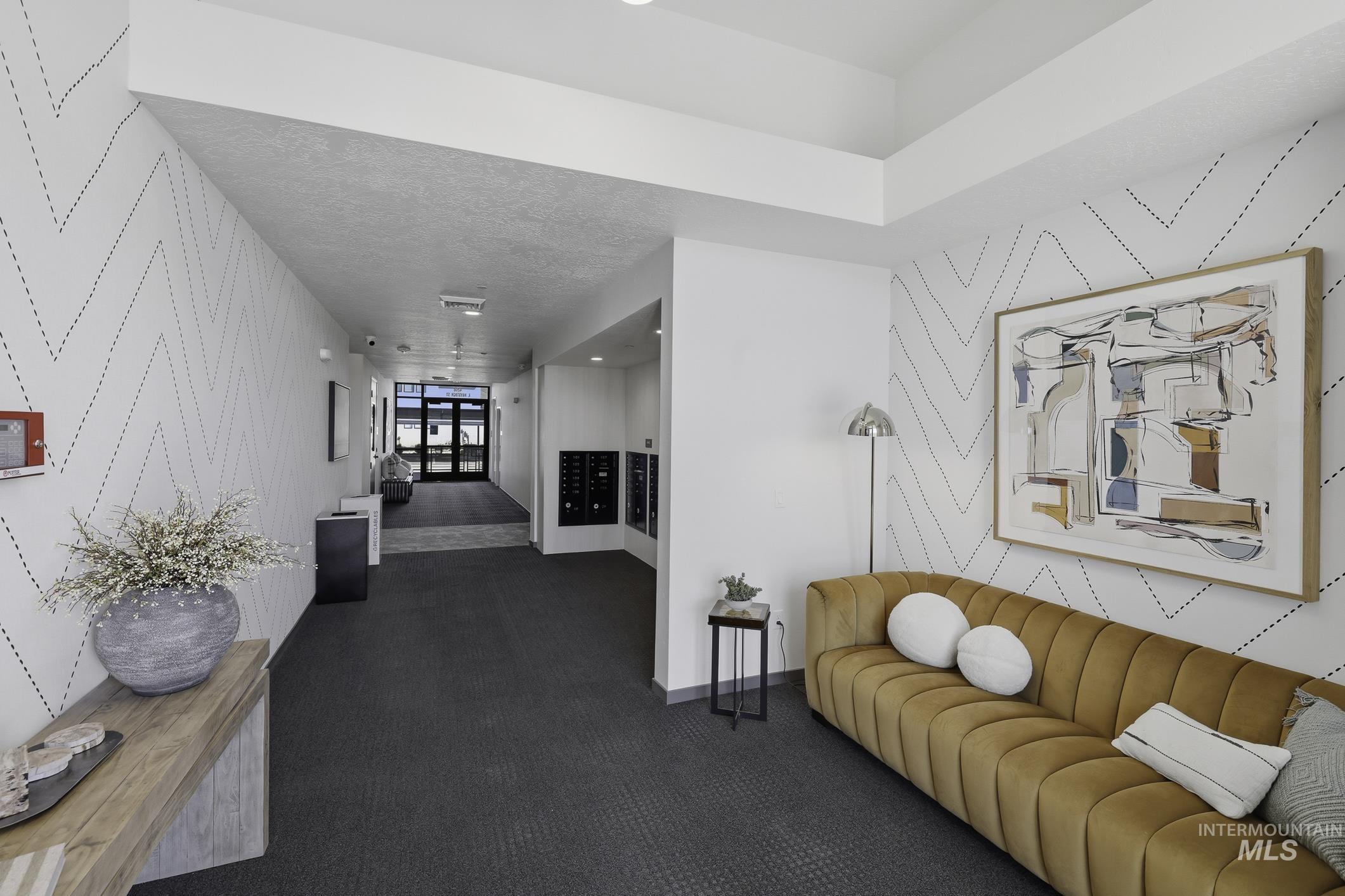 Hallway featuring an accent wall, wallpapered walls, and dark colored carpet