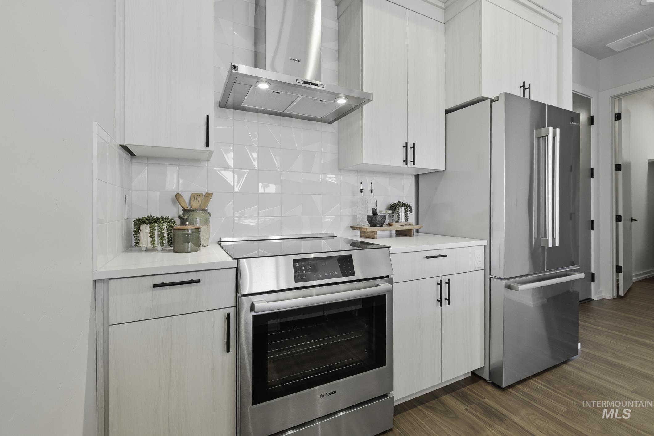 Kitchen with stainless steel appliances, light stone counters, dark wood-style flooring, and white cabinets