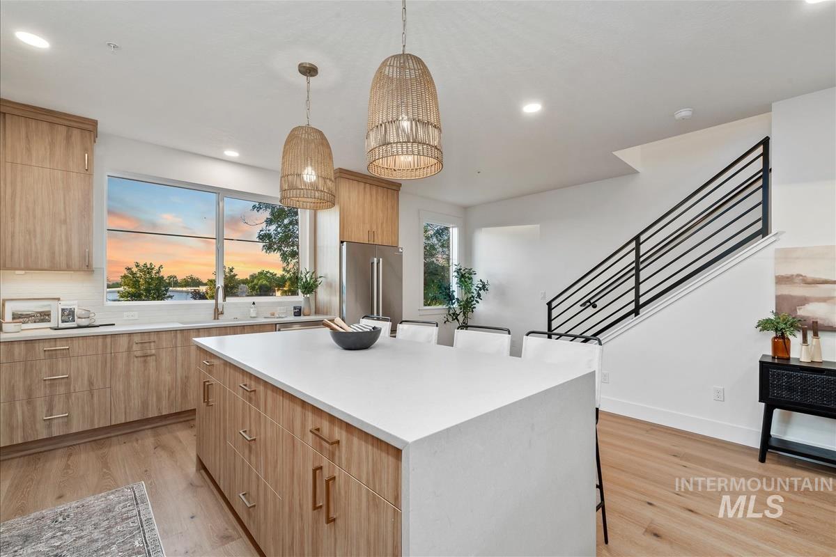 Kitchen with light wood-type flooring, a kitchen island, recessed lighting, high end fridge, and hanging light fixtures