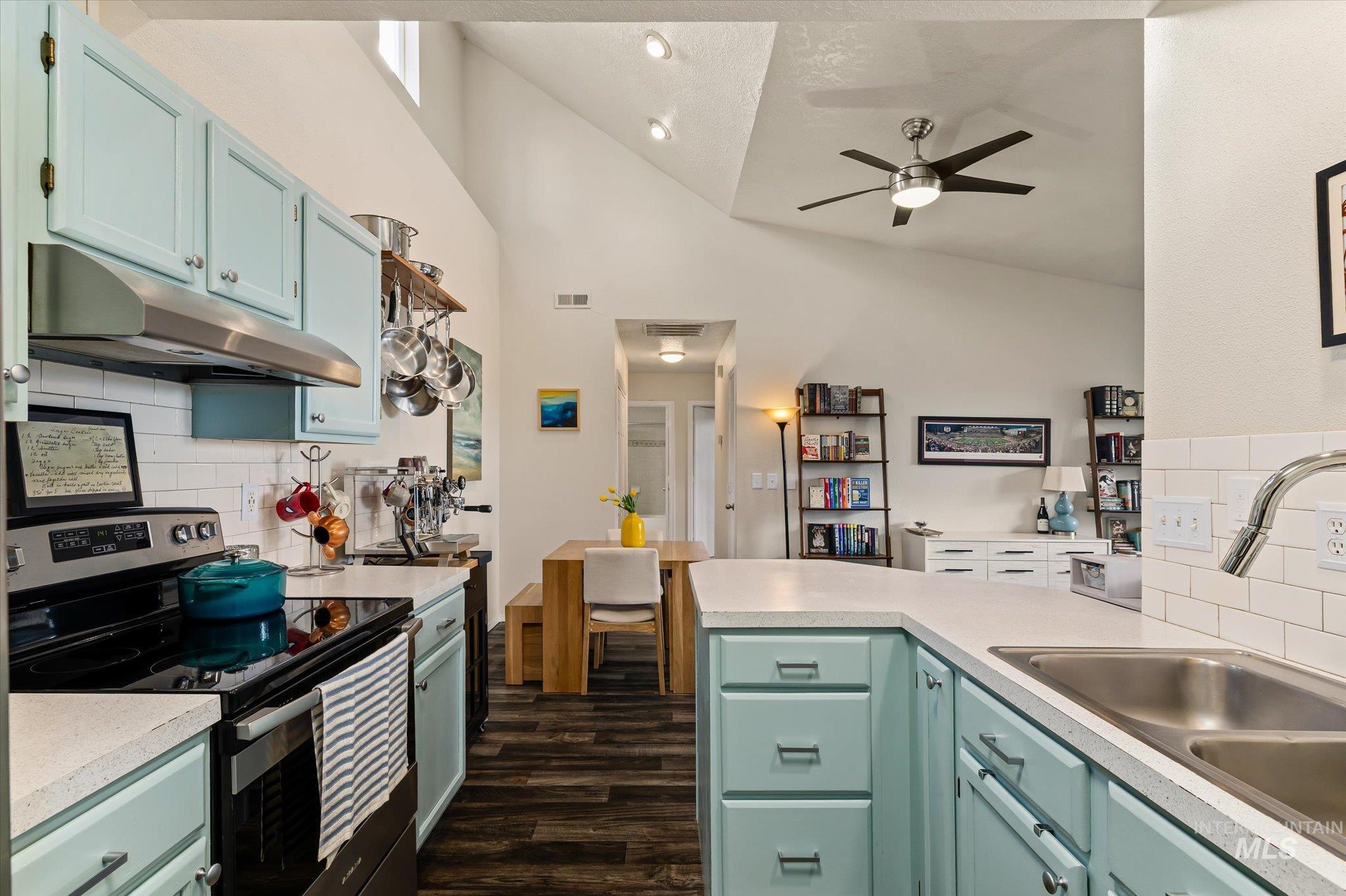 Kitchen with backsplash, stainless steel electric stove, under cabinet range hood, light countertops, and high vaulted ceiling