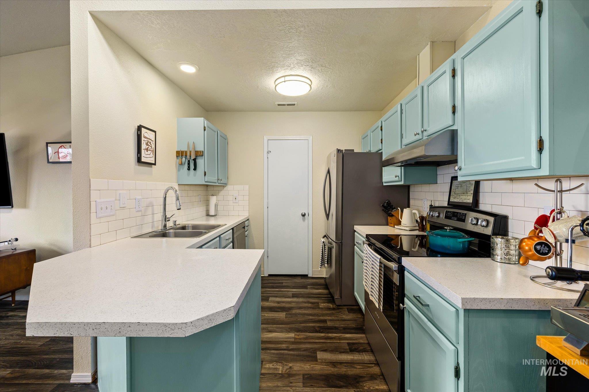 Kitchen featuring stainless steel appliances, light countertops, a peninsula, a textured ceiling, and dark wood-type flooring