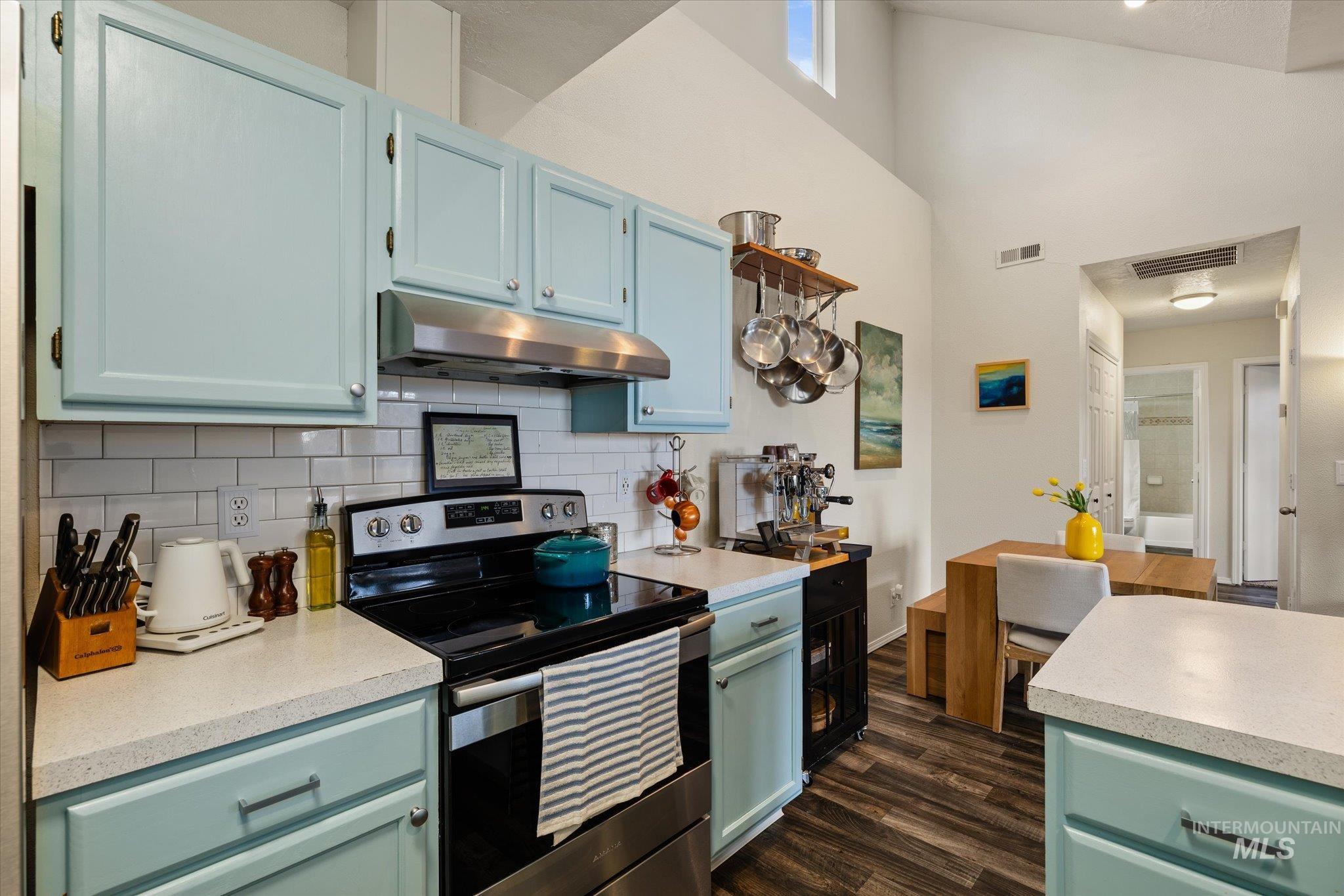 Kitchen with stainless steel electric stove, light countertops, high vaulted ceiling, under cabinet range hood, and dark wood finished floors