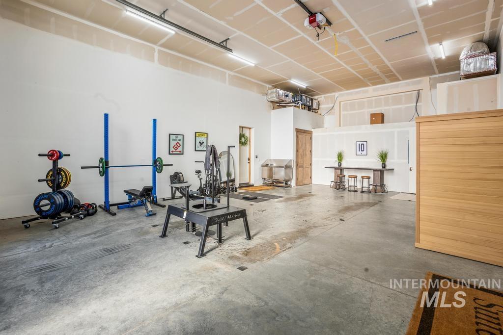 Spacious garage with concrete flooring, exposed ceiling joists, linear overhead lighting, and an overhead door mechanism