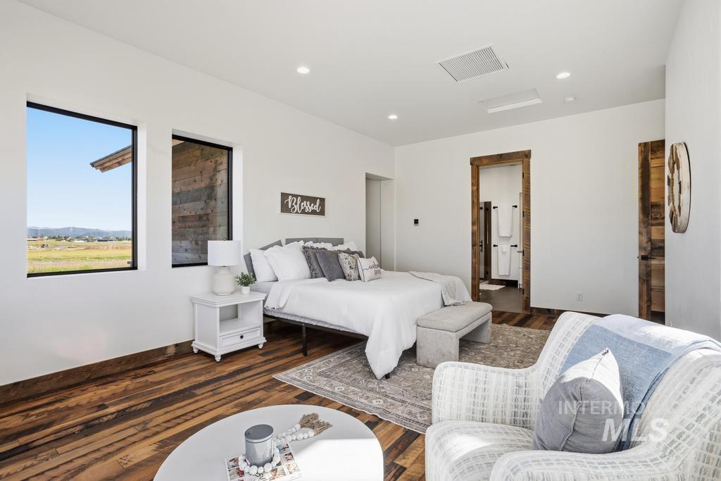 Spacious room featuring wood-finish flooring, two large windows, recessed lighting, and a doorway with rustic wood trim leading to an attached bathroom