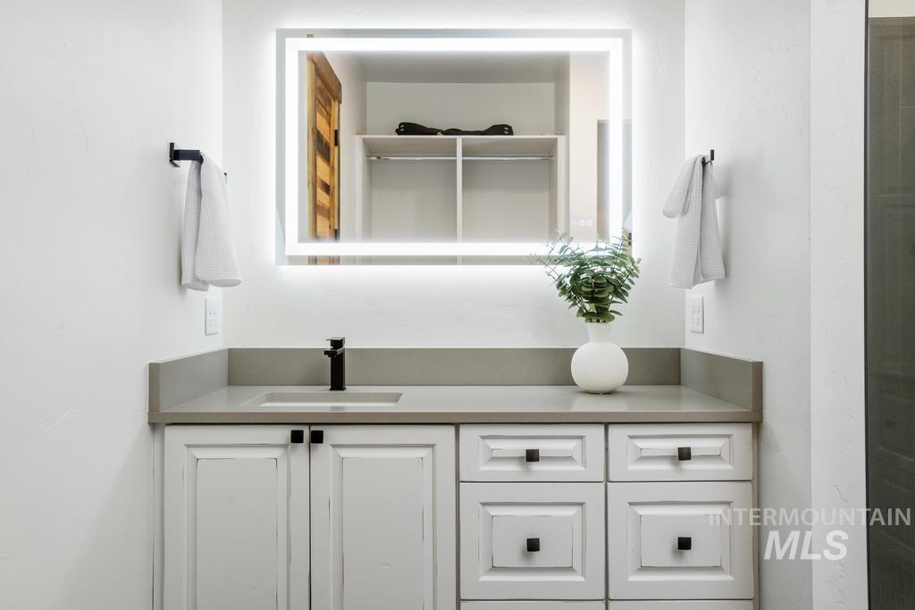 Vanity featuring a lighted rectangular mirror, matte black faucet, and light-toned countertop