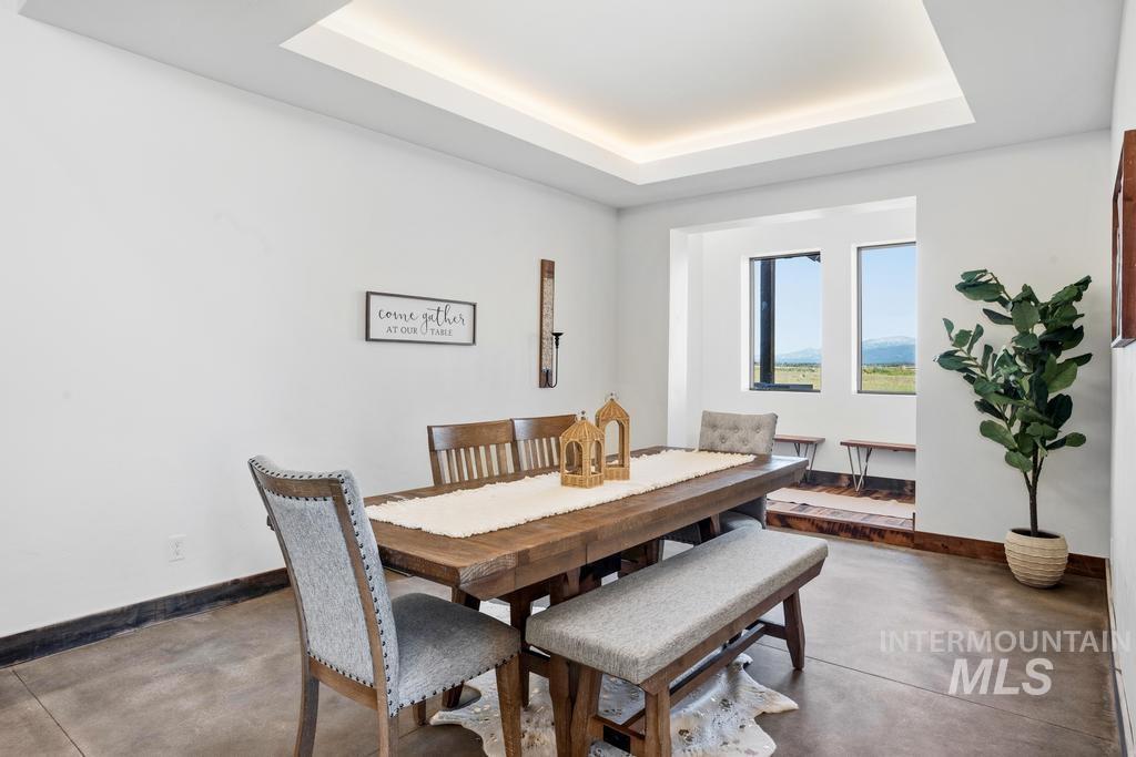 Spacious dining area featuring a tray ceiling with recessed lighting, large windows, stained concrete flooring, and a window seat
