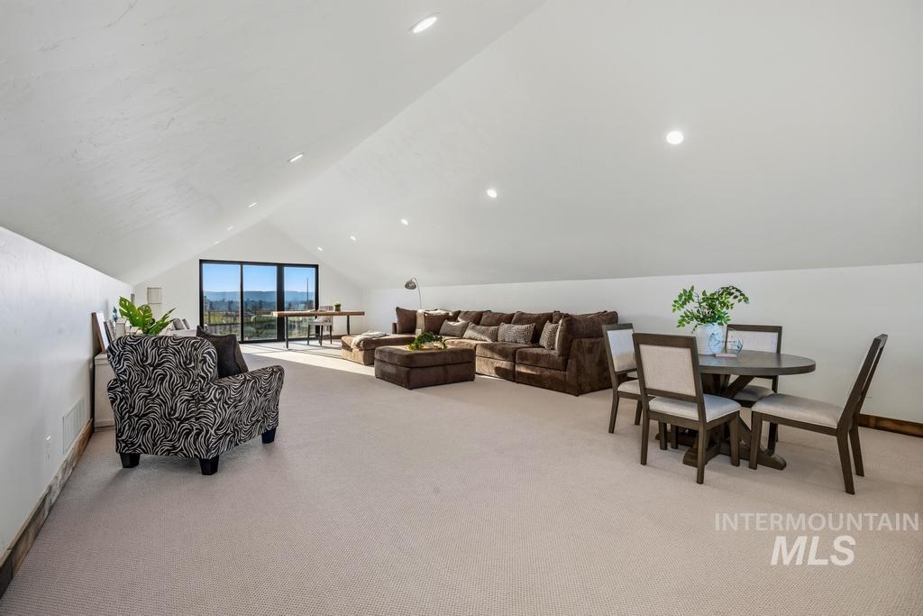 Spacious loft area featuring a sloped ceiling with recessed lighting, light-colored carpeting, and a wall of glass sliding doors