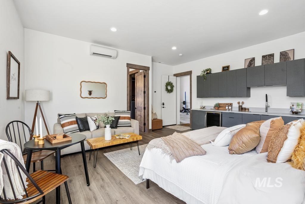 Open-concept studio featuring wood-finish flooring, recessed lighting, a built-in kitchenette with gray cabinetry, and a separate room accessible via a white door