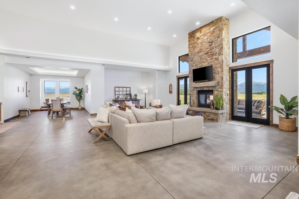 Spacious open-concept living area featuring concrete flooring, a floor-to-ceiling stone fireplace, and high ceilings with recessed lighting