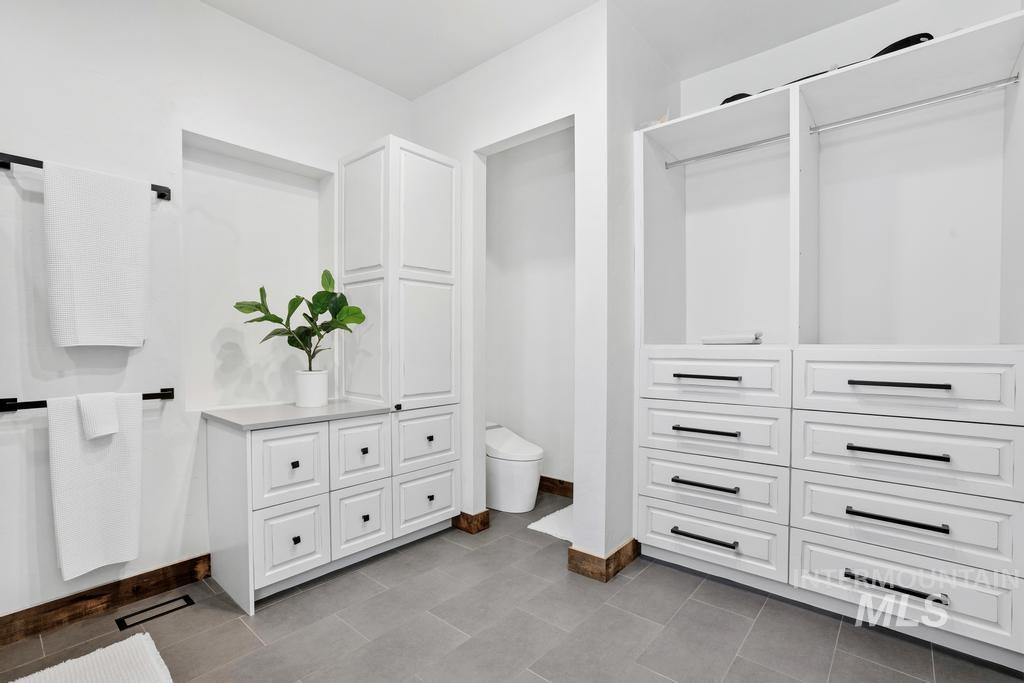 Custom white cabinetry and built-in drawers with matte black hardware, tiled flooring, and a quartz countertop