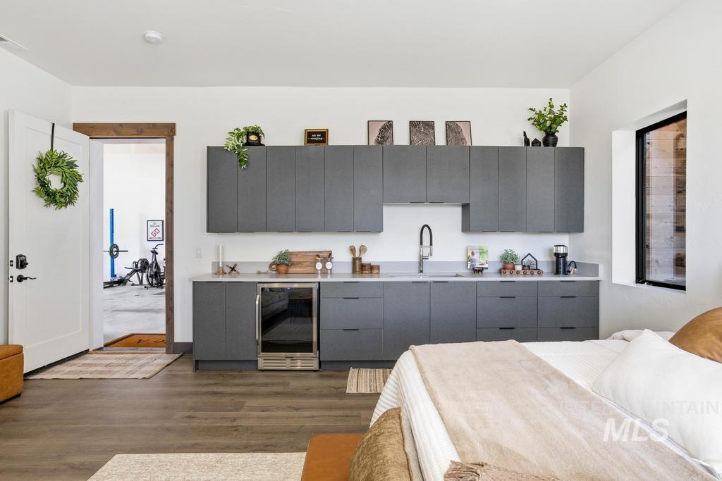 Kitchenette featuring gray flat-panel cabinetry, light-toned countertops, a stainless steel sink with a gooseneck faucet, an under-counter beverage refrigerator, and wood-finish flooring