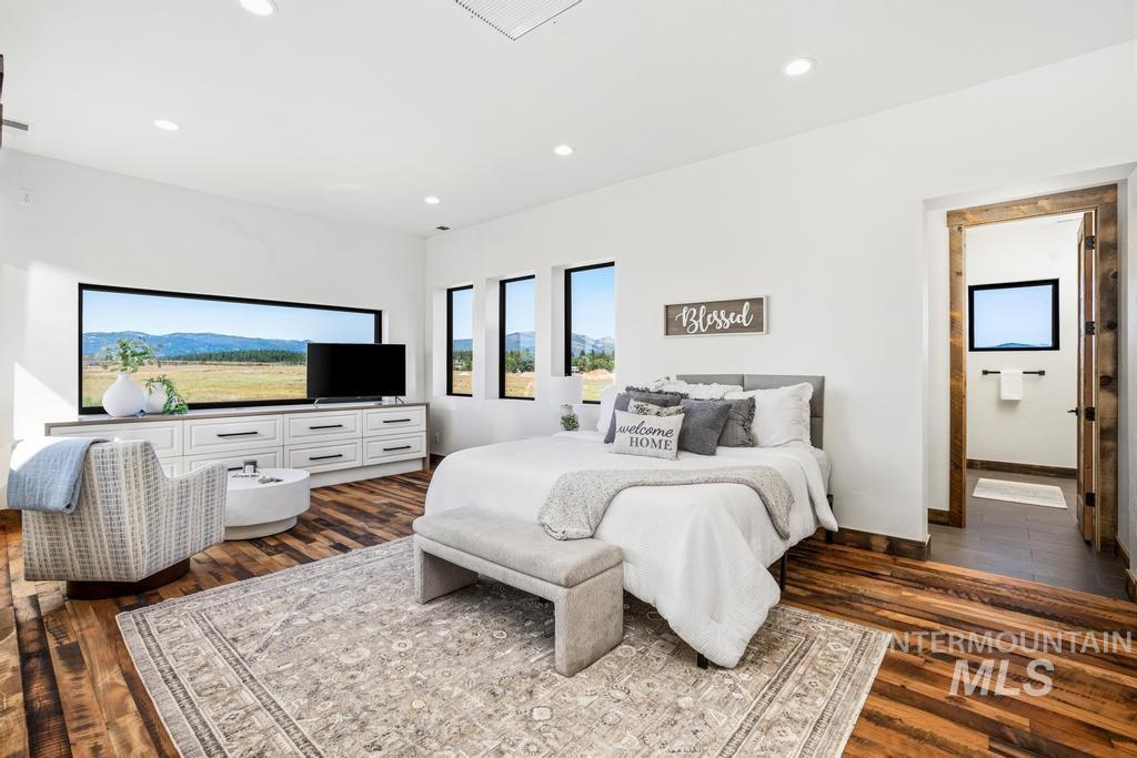 Spacious bedroom featuring wide plank wood-finish flooring, recessed lighting, and a prominent horizontal window offering panoramic scenery