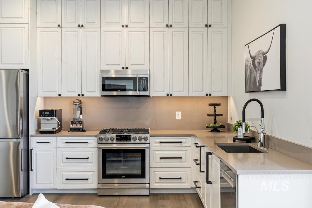 Modern kitchen featuring white shaker cabinetry, stainless steel appliances, stone countertops, and a matte black faucet