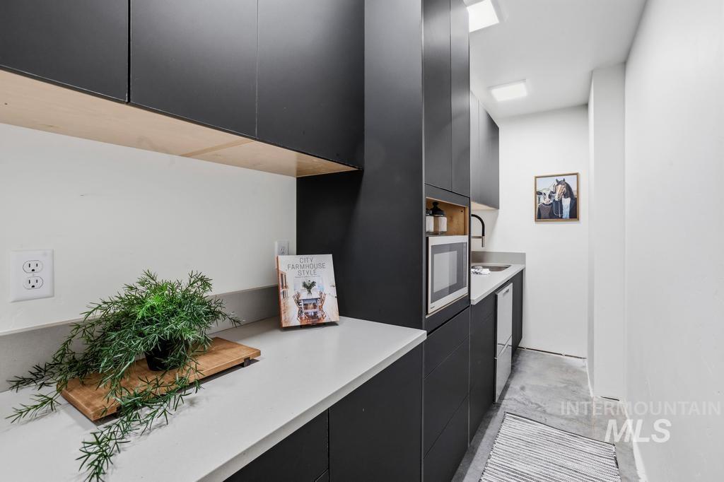 Butlers Pantry featuring matte black cabinetry with light wood accents, light stone countertops, integrated microwave, and a compact sink with a matte black faucet