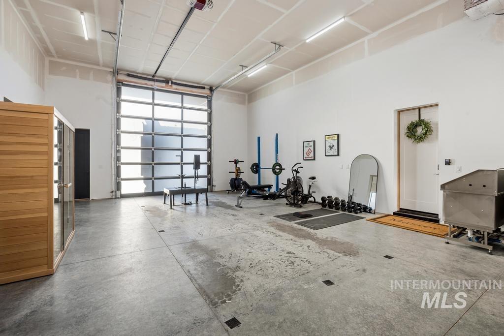 Spacious multi-use area featuring a large glass-paneled roll-up door, high ceilings with exposed conduit, and concrete flooring