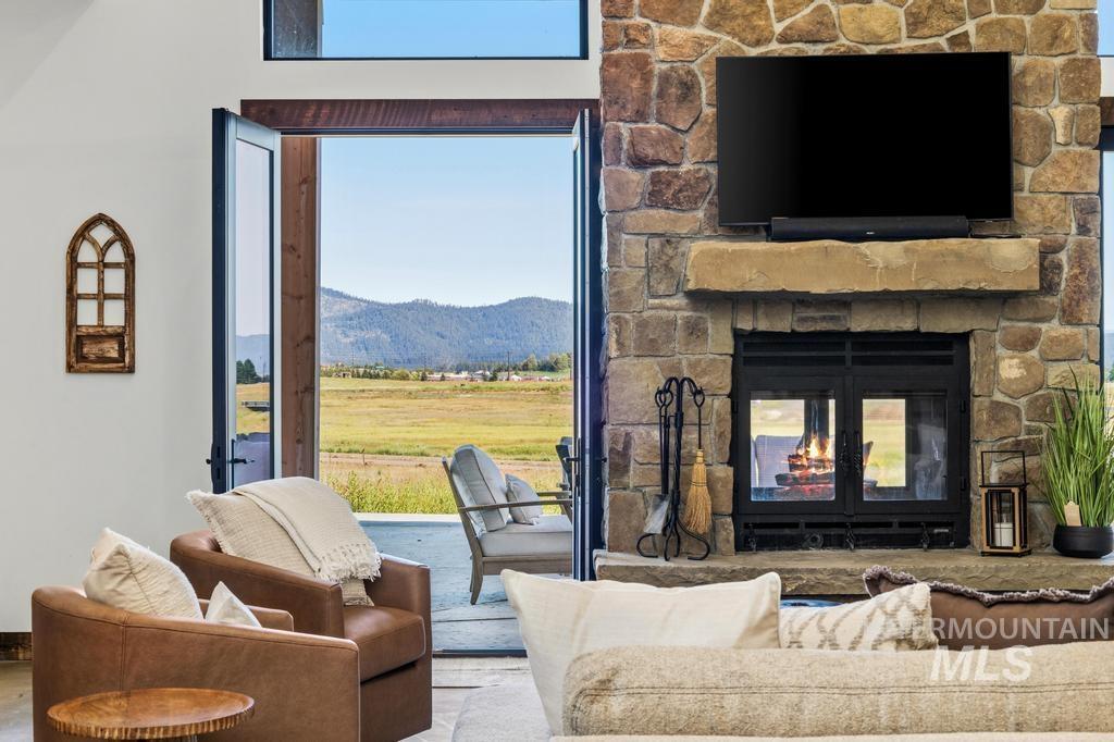 Stone-clad fireplace featuring a substantial mantelpiece and a built-in firebox, complemented by expansive glass doors opening to a concrete patio and a broad, flat landscape