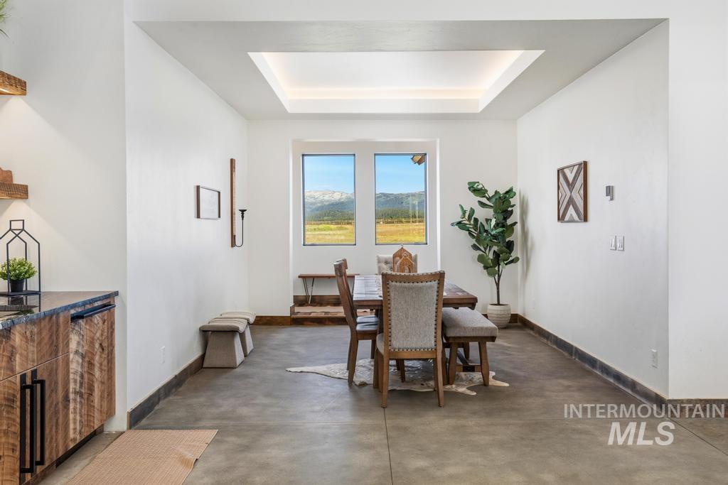 Dining area featuring an illuminated tray ceiling, expansive window with mountain scenery, concrete flooring, and a built-in wood-finish cabinet with a stone countertop
