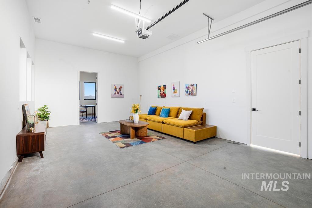 Spacious room featuring concrete flooring, white walls, multiple windows, and a white interior door with black hardware. Plumbed for easy add of bathroom, room for a kitchenette. Make this a ONE bedroom additional space.