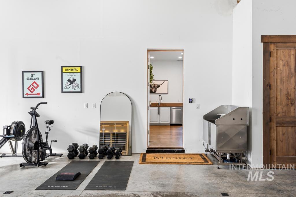 Open concept space with concrete flooring, high ceilings, a wood-finish door, and a stainless steel utility sink