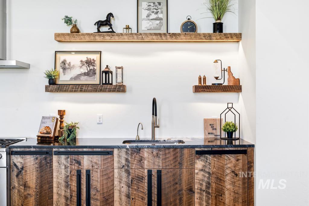 Kitchen featuring distressed wood-finish cabinetry with black hardware, black countertop, and a stainless steel sink with a gooseneck faucet