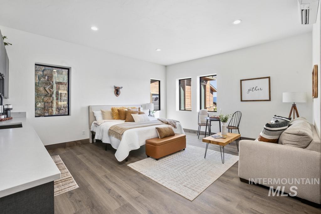 Spacious studio-style room featuring wood-finish flooring, recessed lighting, white walls, and black-framed windows
