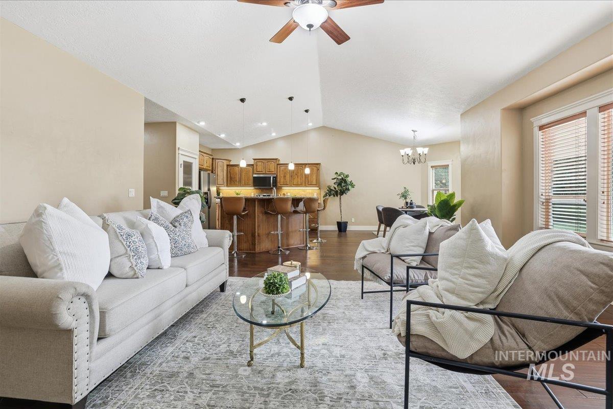 Great room with Living area featuring vaulted ceiling, dark wood-style floors, a ceiling fan, and a chandelier opening to Kitchen and dining