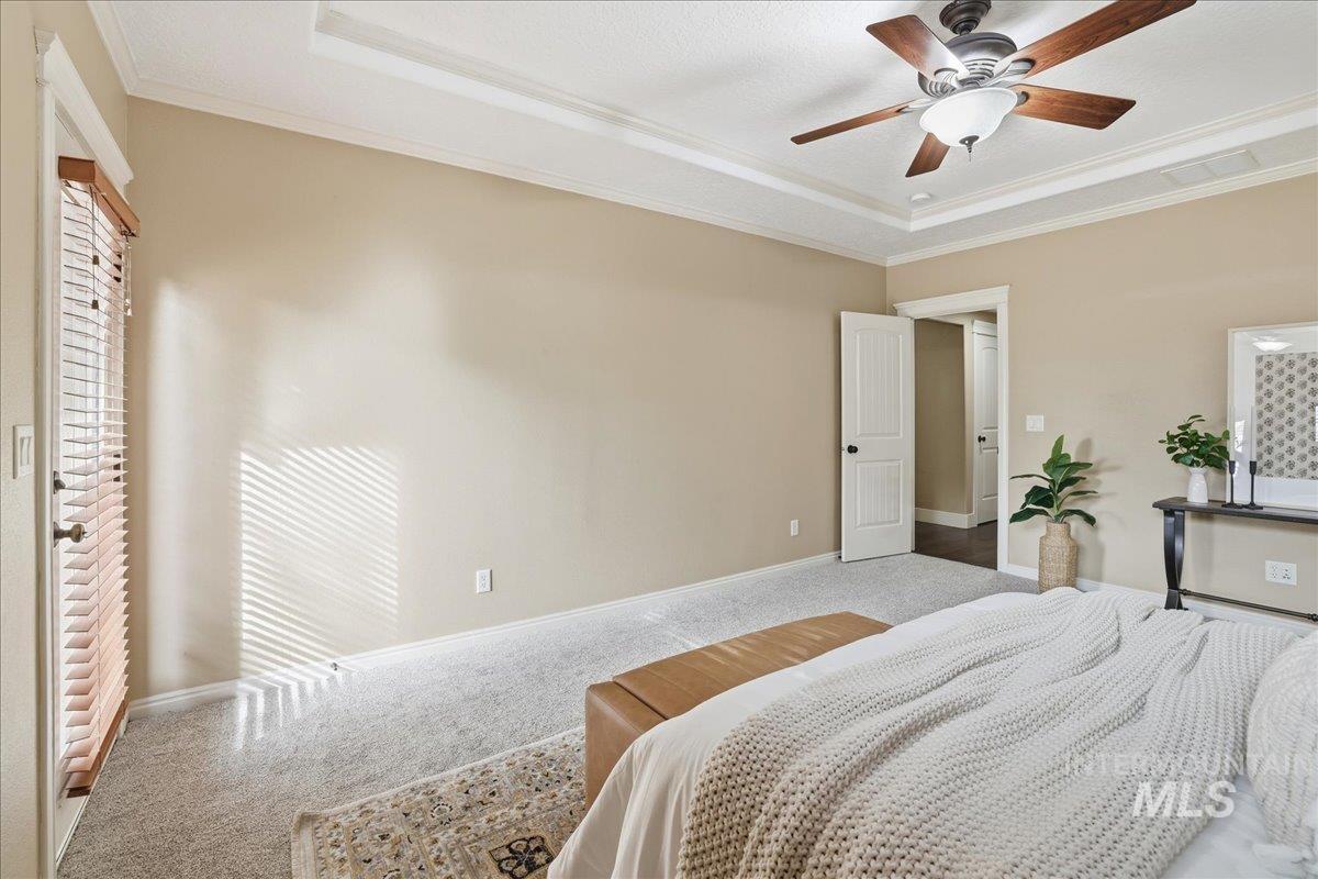 Carpeted bedroom with a raised ceiling, ceiling fan, and ornamental molding