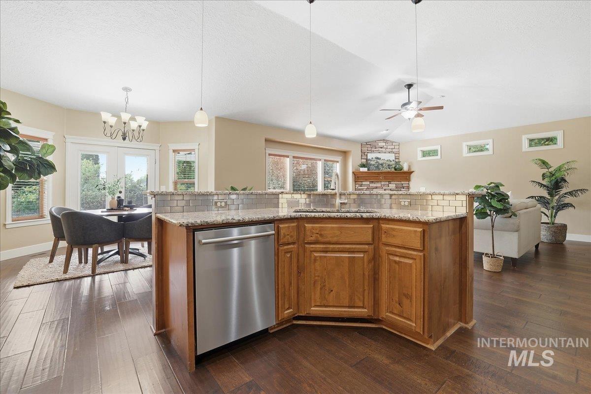 Kitchen featuring brown cabinetry, tasteful backsplash, a center island with sink, stainless steel dishwasher, and dark wood-style floors