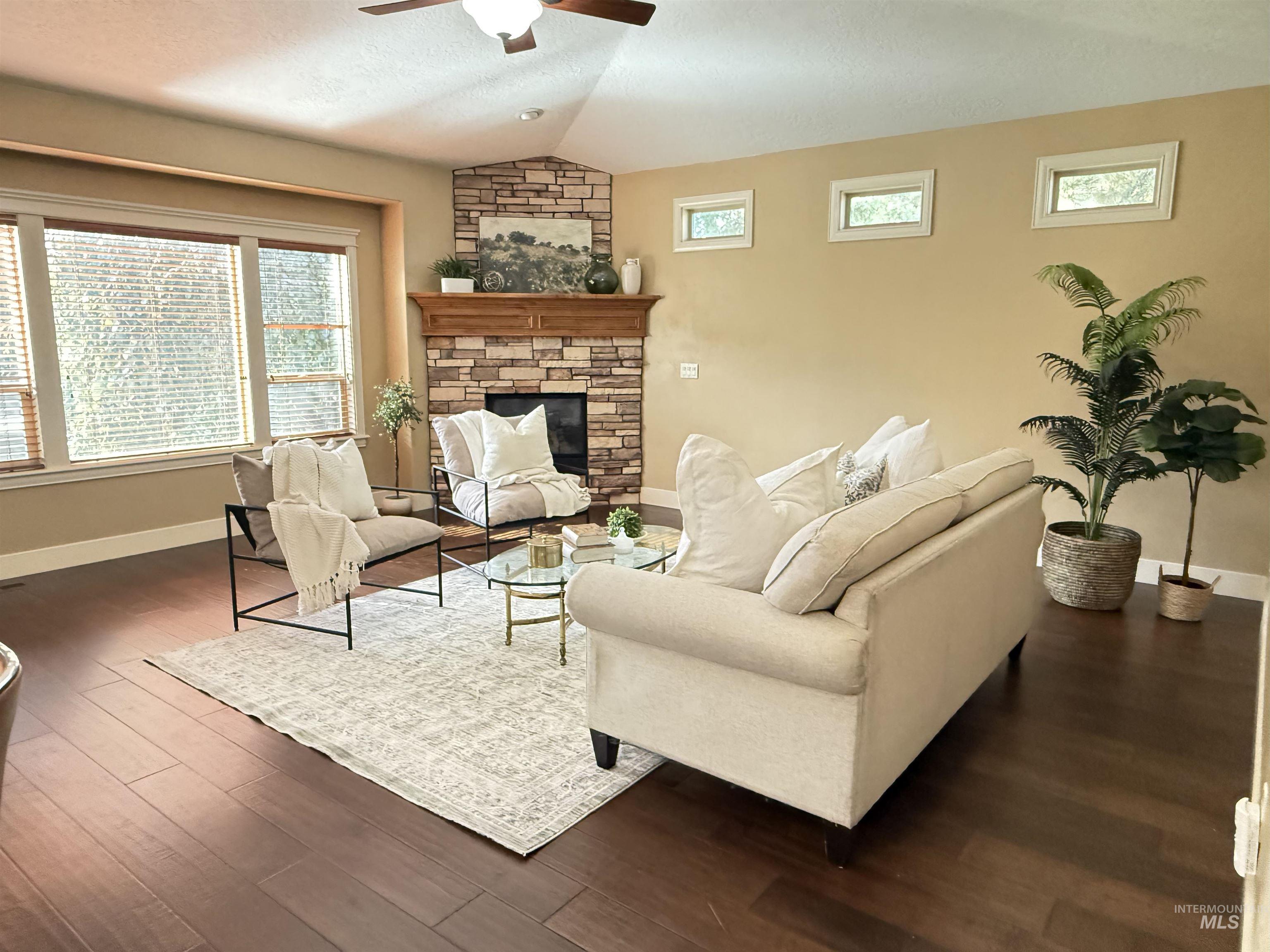 Living area featuring plenty of natural light, lofted ceiling, a stone fireplace, dark wood finished floors, and ceiling fan