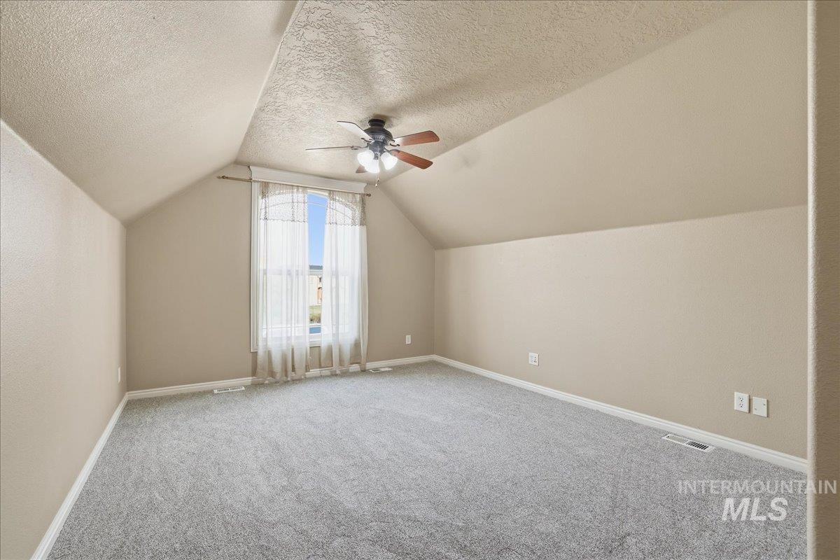 Bonus room featuring carpet floors, lofted ceiling, a textured ceiling, and a ceiling fan