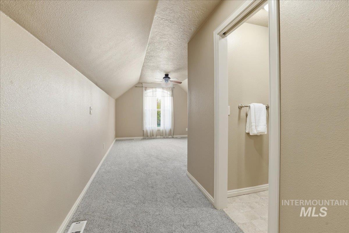 Bonus room featuring a textured ceiling, a textured wall, vaulted ceiling, light carpet, and ceiling fan