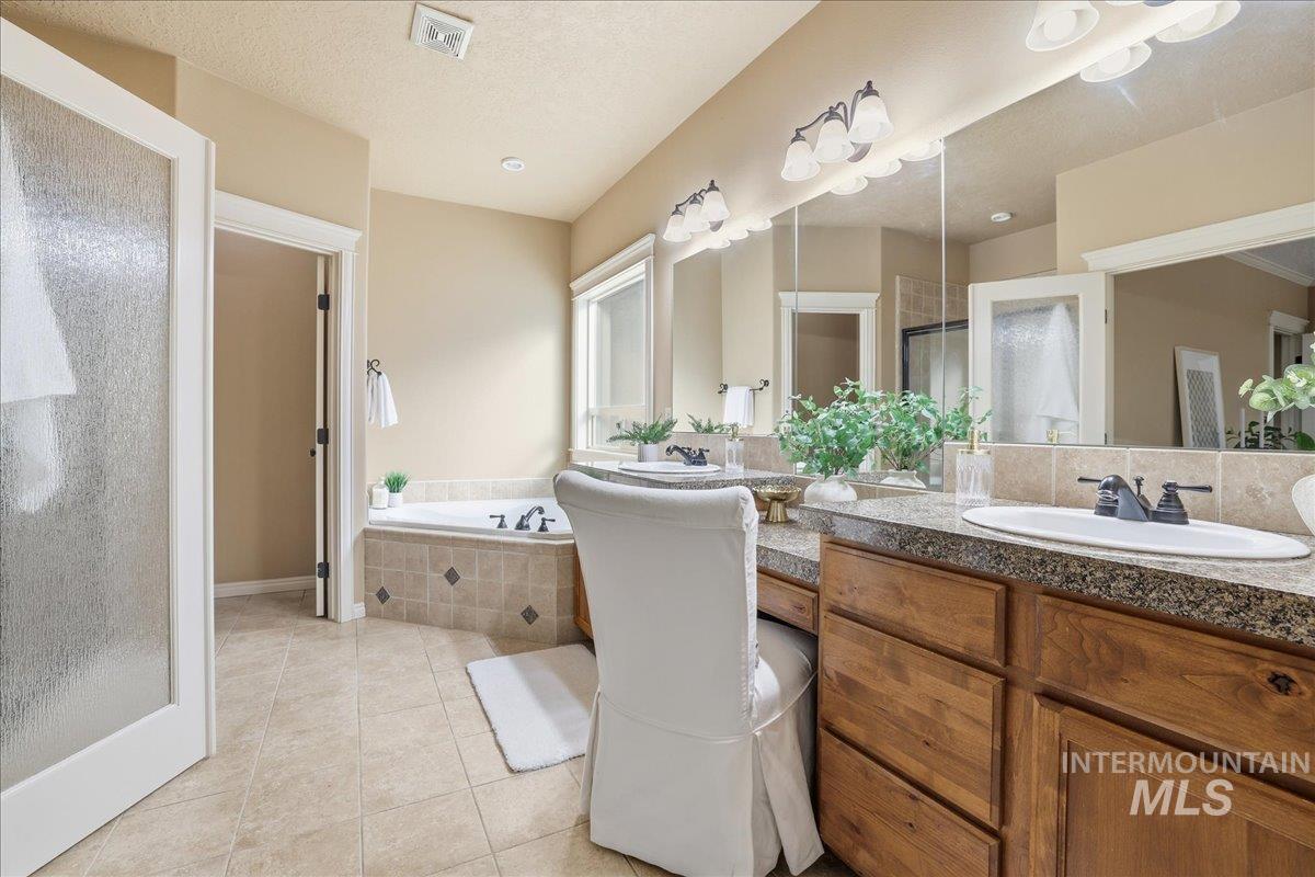 Full bathroom featuring light tile patterned floors, a garden tub, double vanity, a stall shower, and a textured ceiling