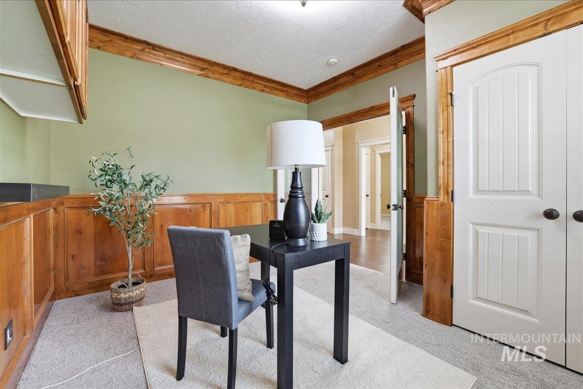 Office area featuring a textured ceiling, a wainscoted wall, light carpet, and wooden walls