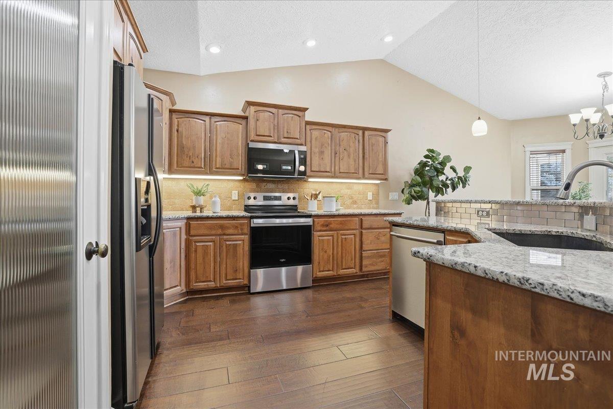 Kitchen featuring decorative backsplash, appliances with stainless steel finishes, a textured ceiling, brown cabinetry, and hanging light fixtures
