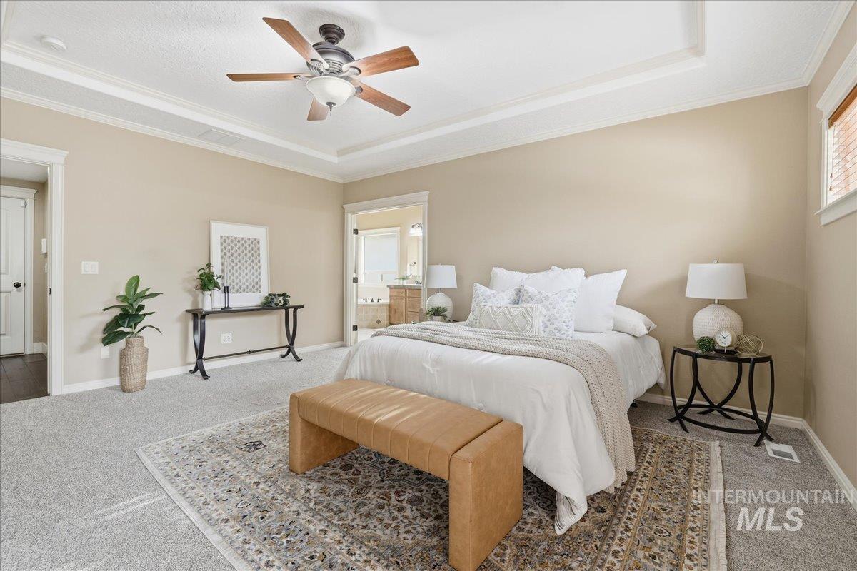 Carpeted bedroom featuring a tray ceiling, crown molding, connected bathroom, and ceiling fan