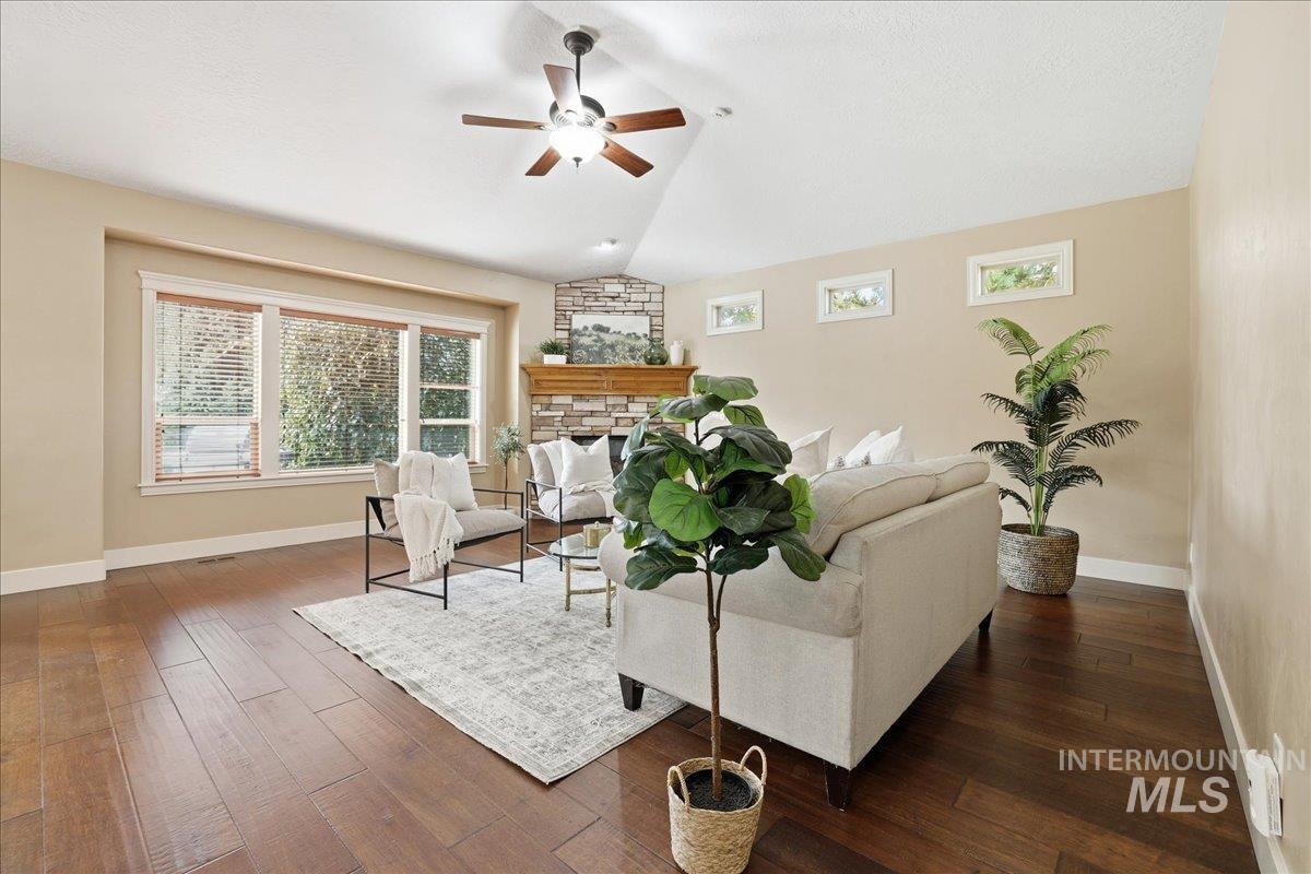 Living area featuring vaulted ceiling, dark wood-style floors, a fireplace, and ceiling fan