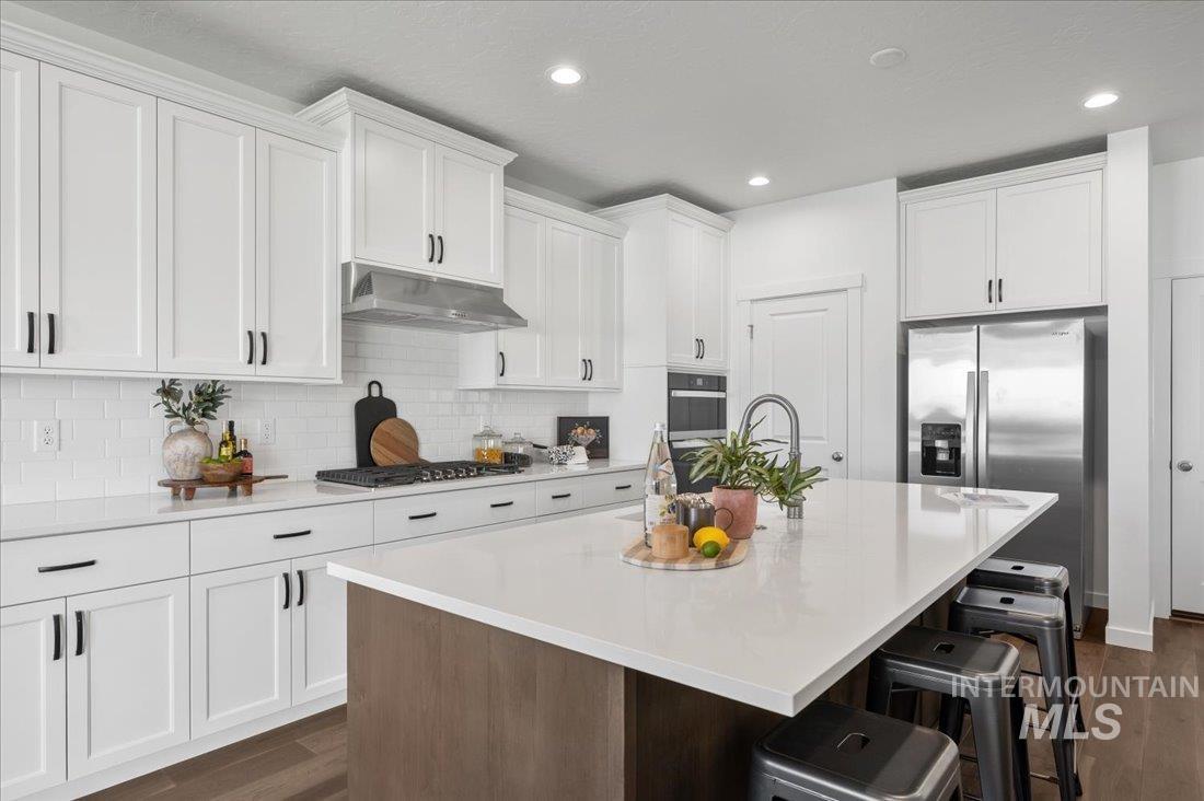 Two tone kitchen with a kitchen breakfast bar, a kitchen island with sink, stainless steel appliances, dark wood finished floors, and light stone counters