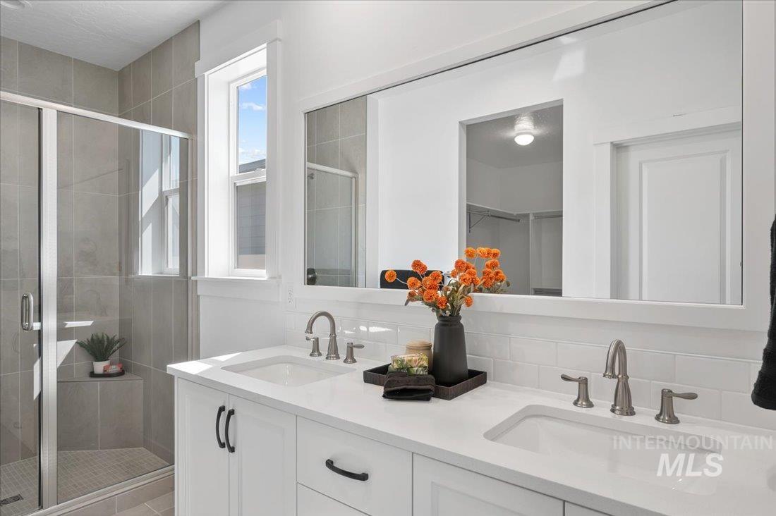 Full bathroom with double vanity, a stall shower, a walk in closet, and backsplash