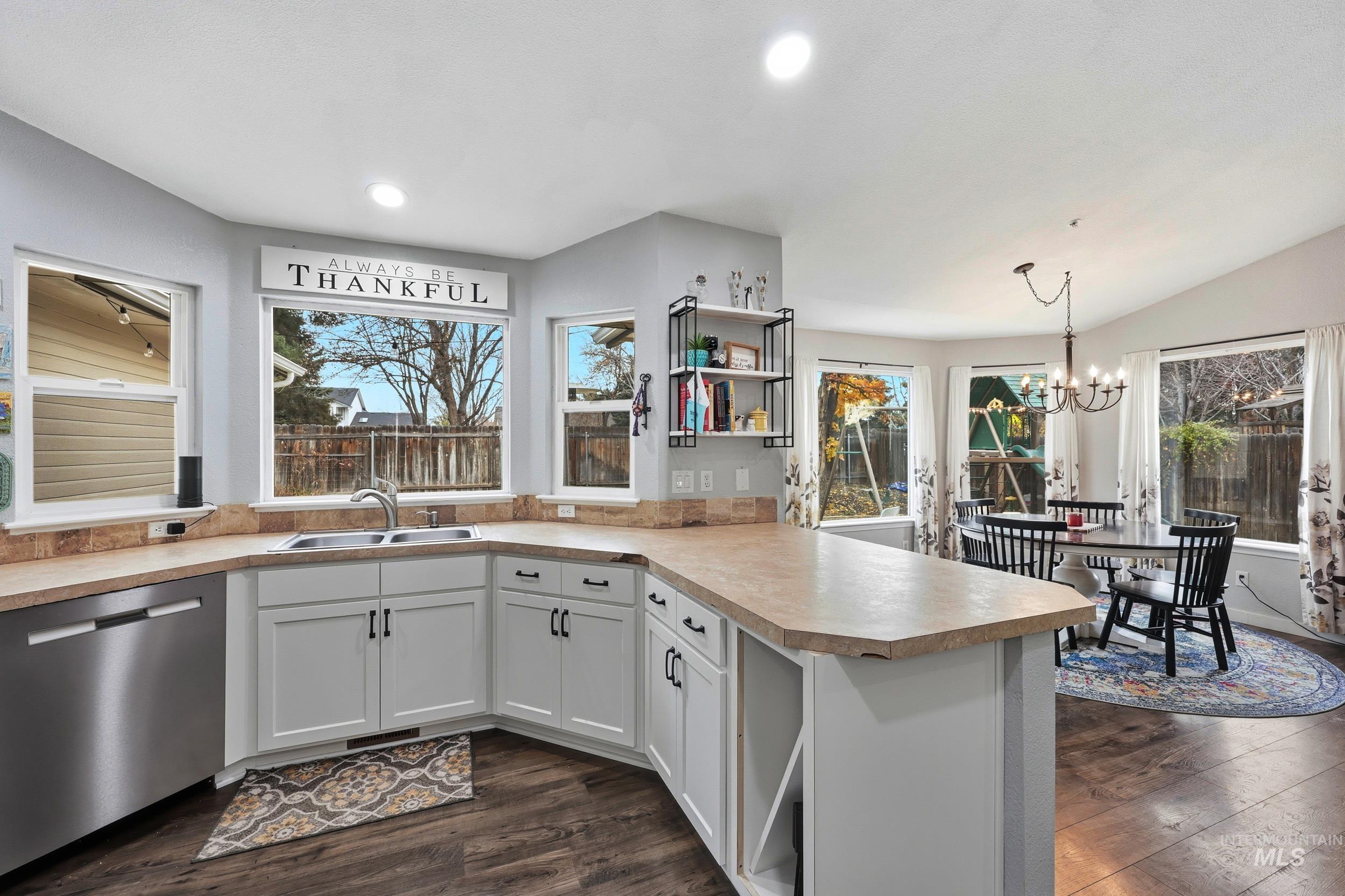 Kitchen featuring dishwasher, white cabinetry, decorative light fixtures, dark wood finished floors, and a peninsula