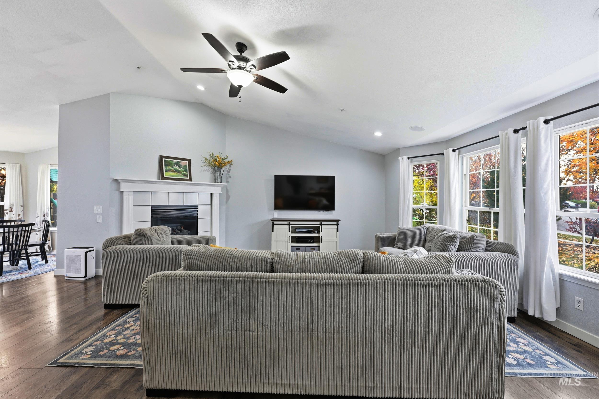 Living room with lofted ceiling, healthy amount of natural light, dark wood finished floors, a tile fireplace, and ceiling fan