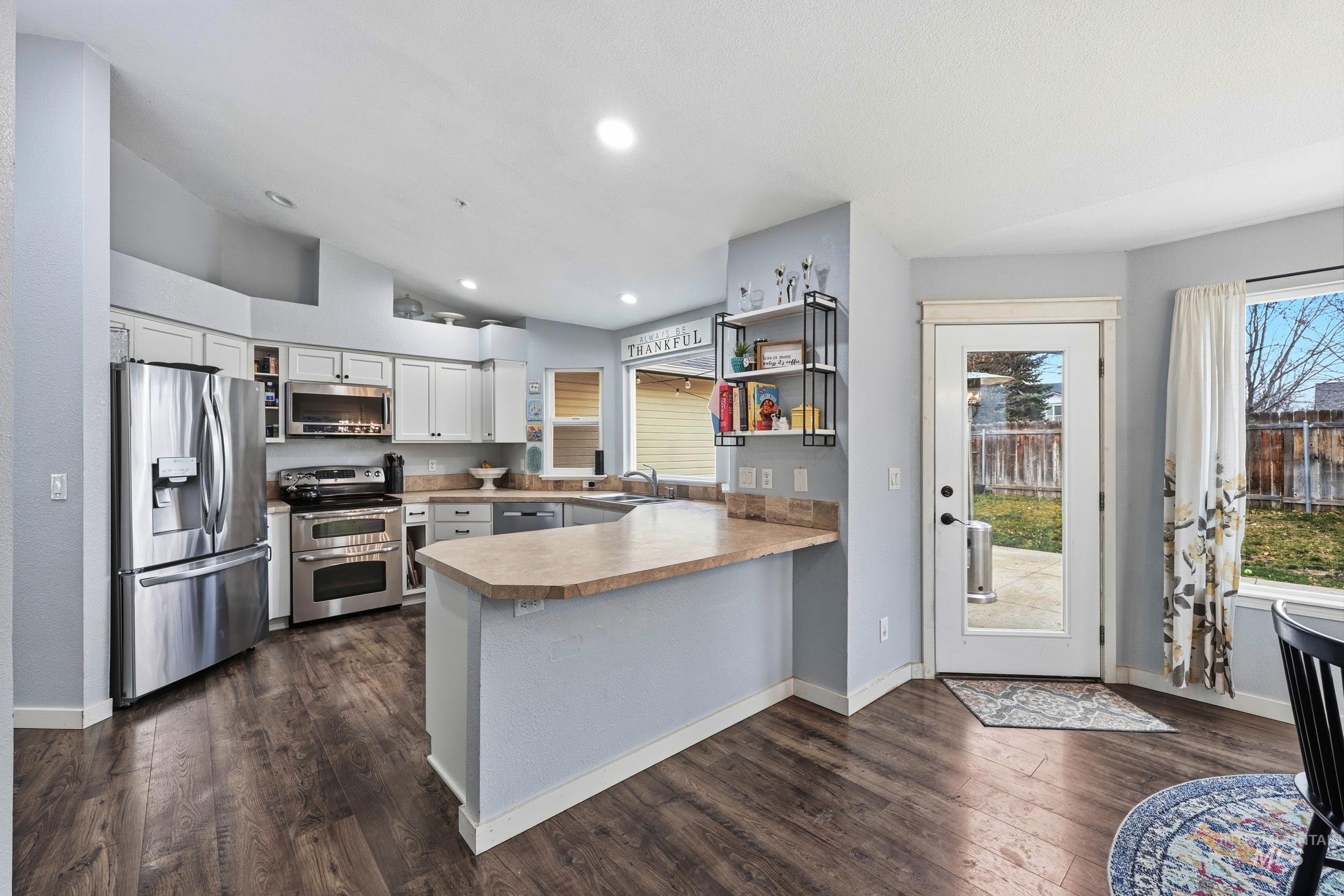Kitchen featuring open shelves, stainless steel appliances, a peninsula, white cabinetry, and light countertops