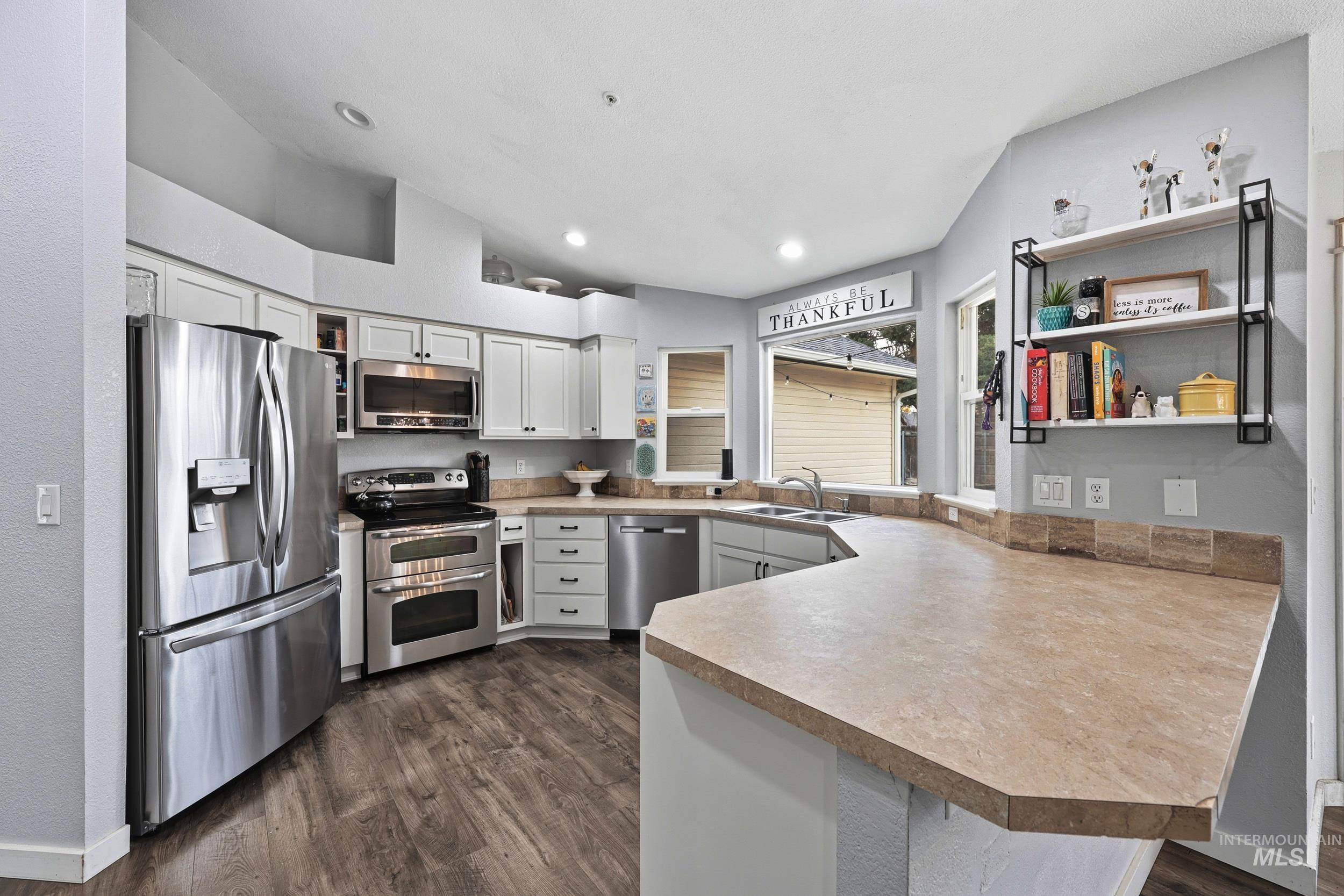Kitchen with a peninsula, stainless steel appliances, dark wood finished floors, light countertops, and lofted ceiling