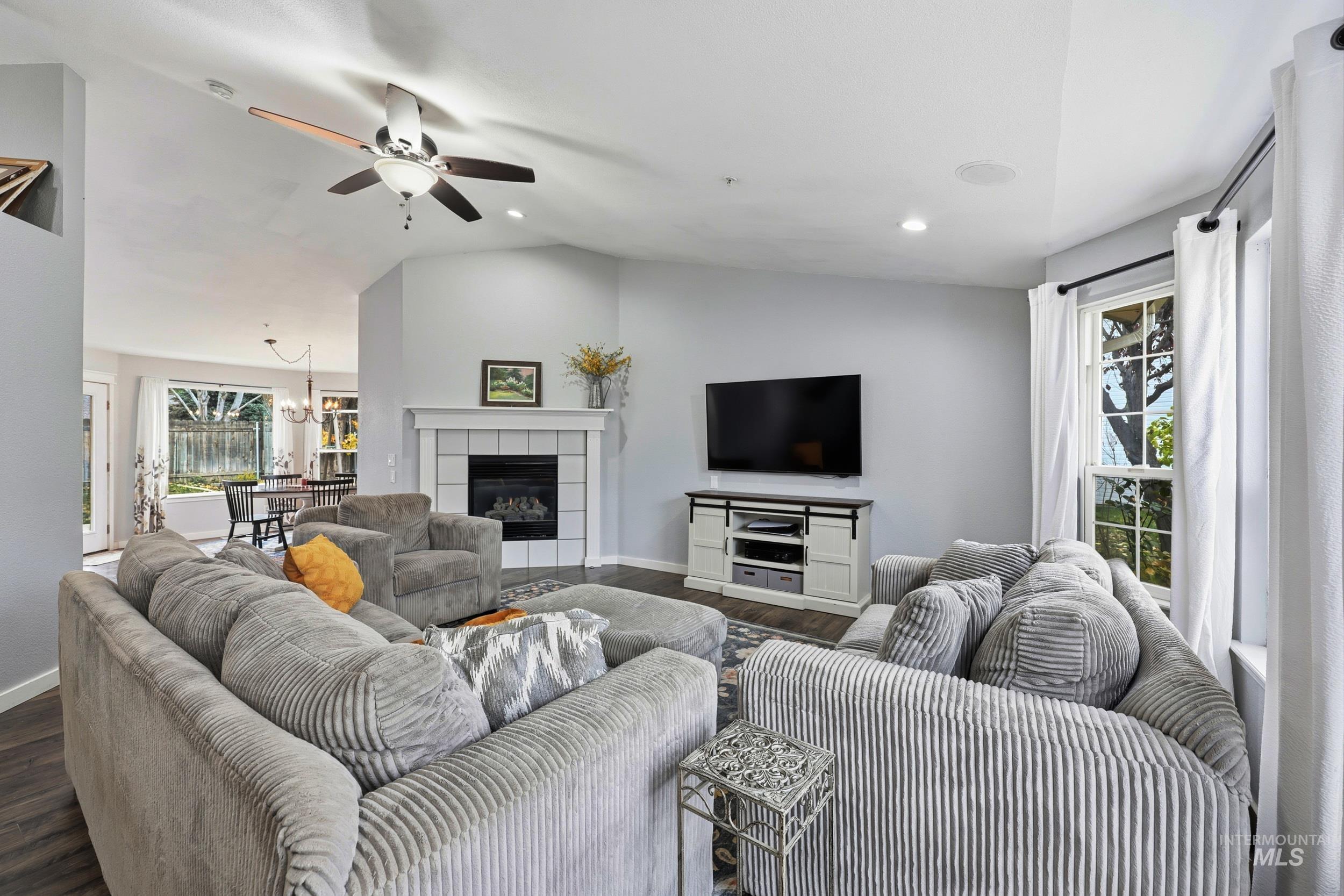 Living room with lofted ceiling, wood finished floors, a ceiling fan, a fireplace, and recessed lighting